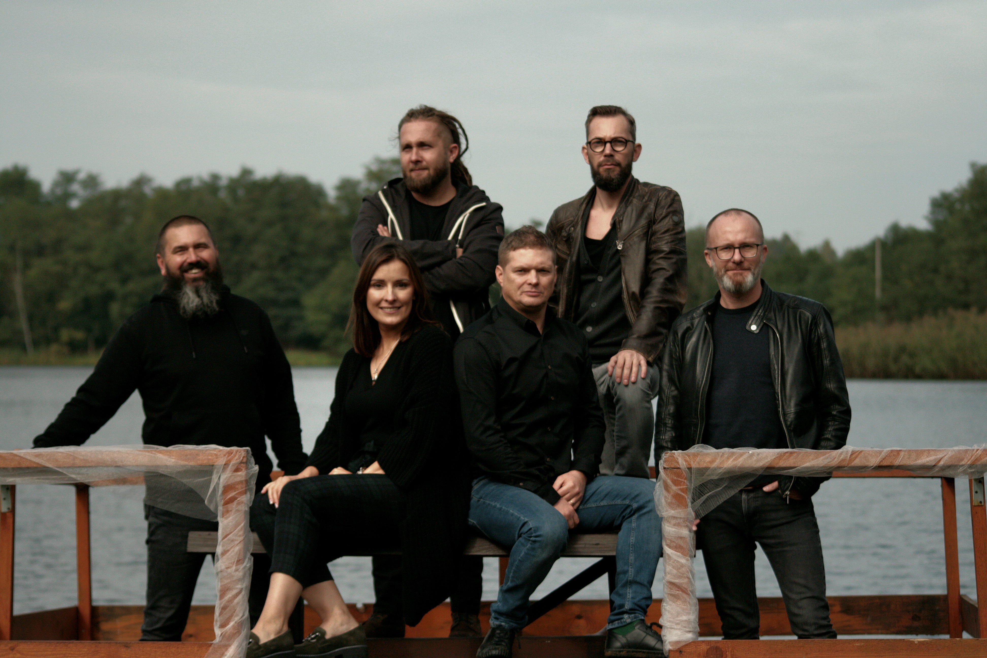 Grupa sześciu os&oacute;b - jednej kobiety i&nbsp;pieciu mężczyzn - pozuje do zdjęcia na&nbsp;tle drzew i&nbsp;jeziora