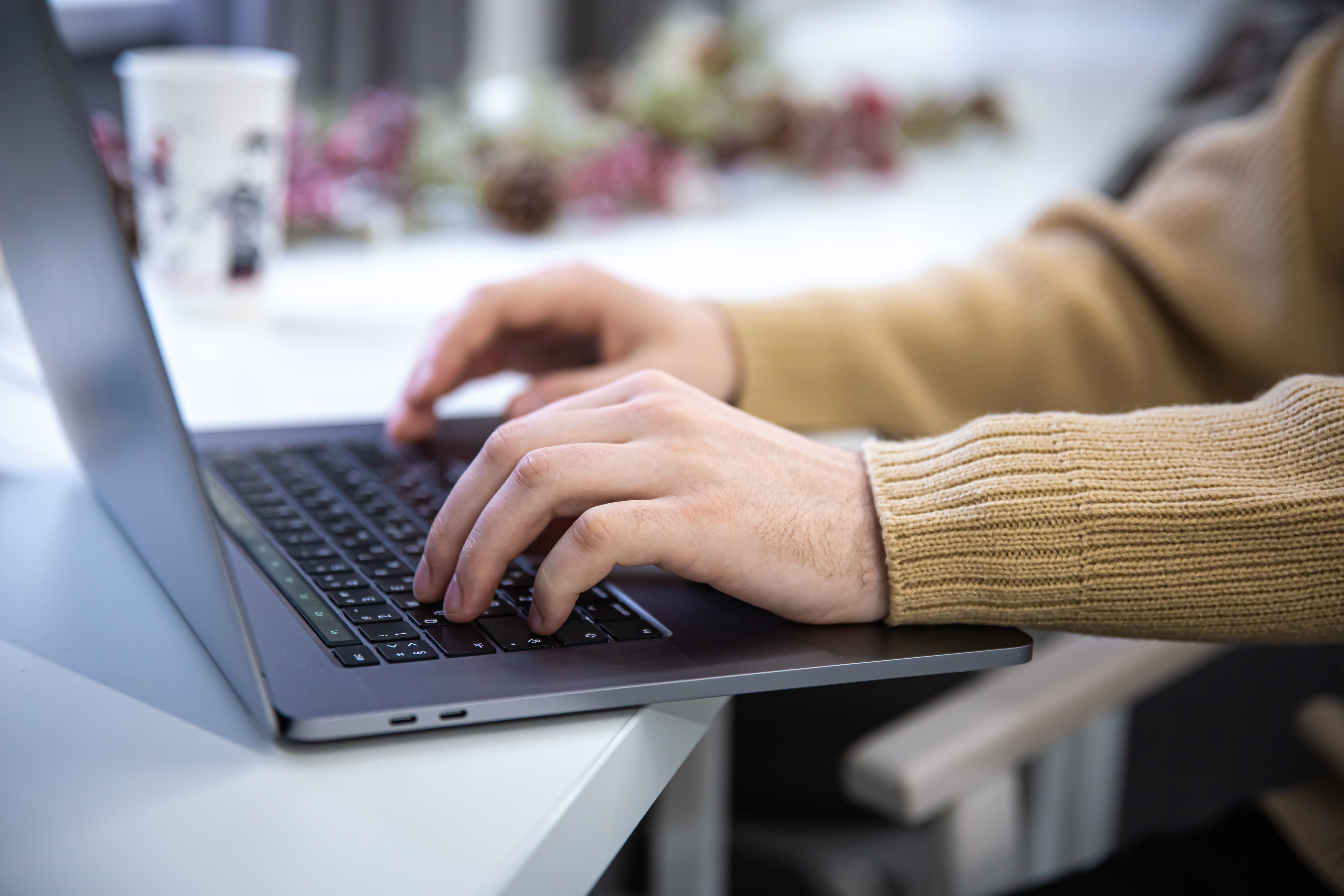 Zbliżenie na&nbsp;parę ludzkich rąk, kt&oacute;re dotykają klawiatury laptopa, stojącego na&nbsp;brzegu stolika