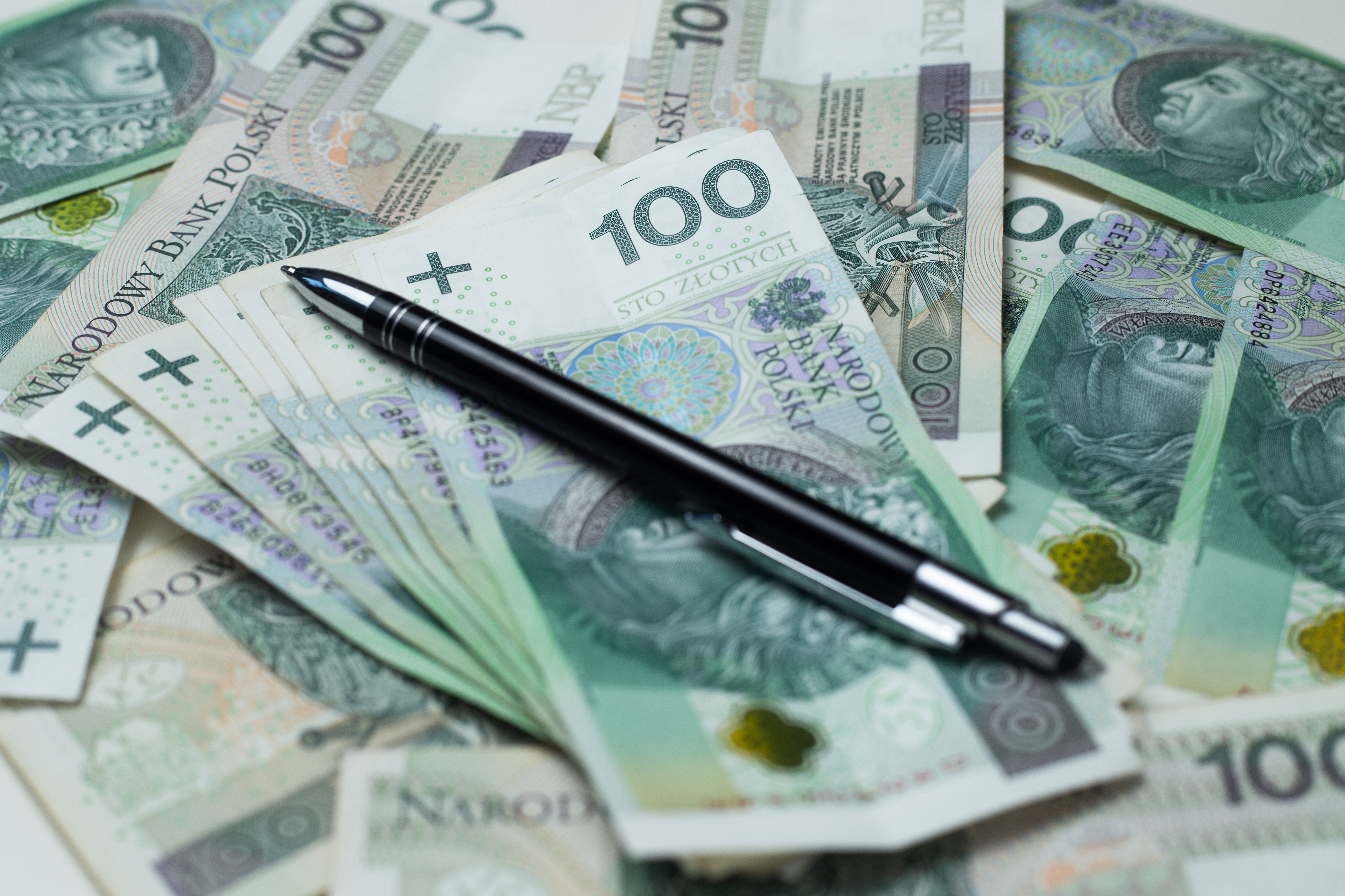 Duża ilość banknot&oacute;w stuzłotowych, na&nbsp;nich położony czarny długopis