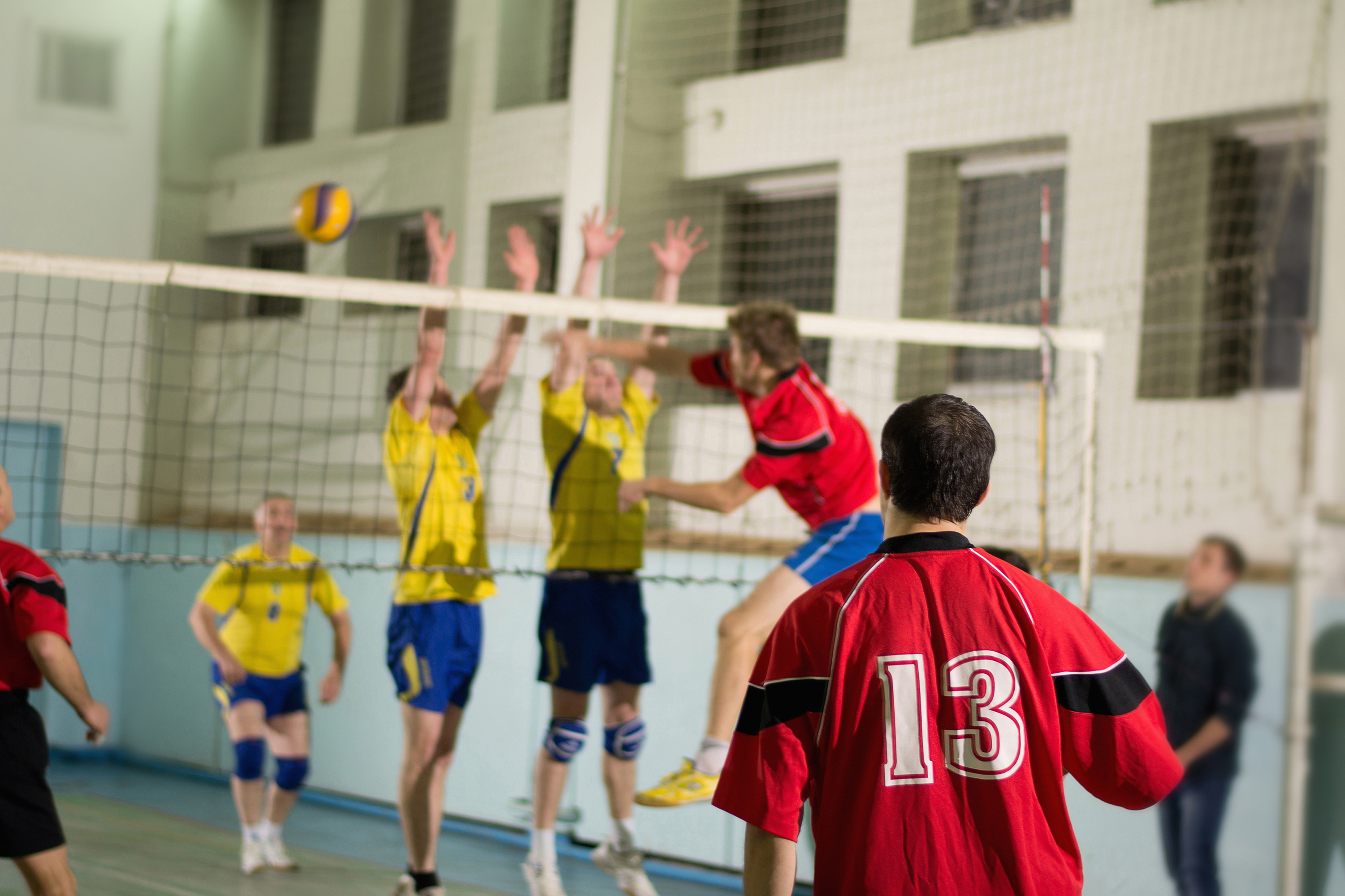 Kilka os&oacute;b na&nbsp;sali sportowej podzielona na&nbsp;dwie drużyny, jedni w&nbsp;ż&oacute;łtych drudzy w&nbsp;czerwonych koszulkach, grają w&nbsp;siatk&oacute;wę