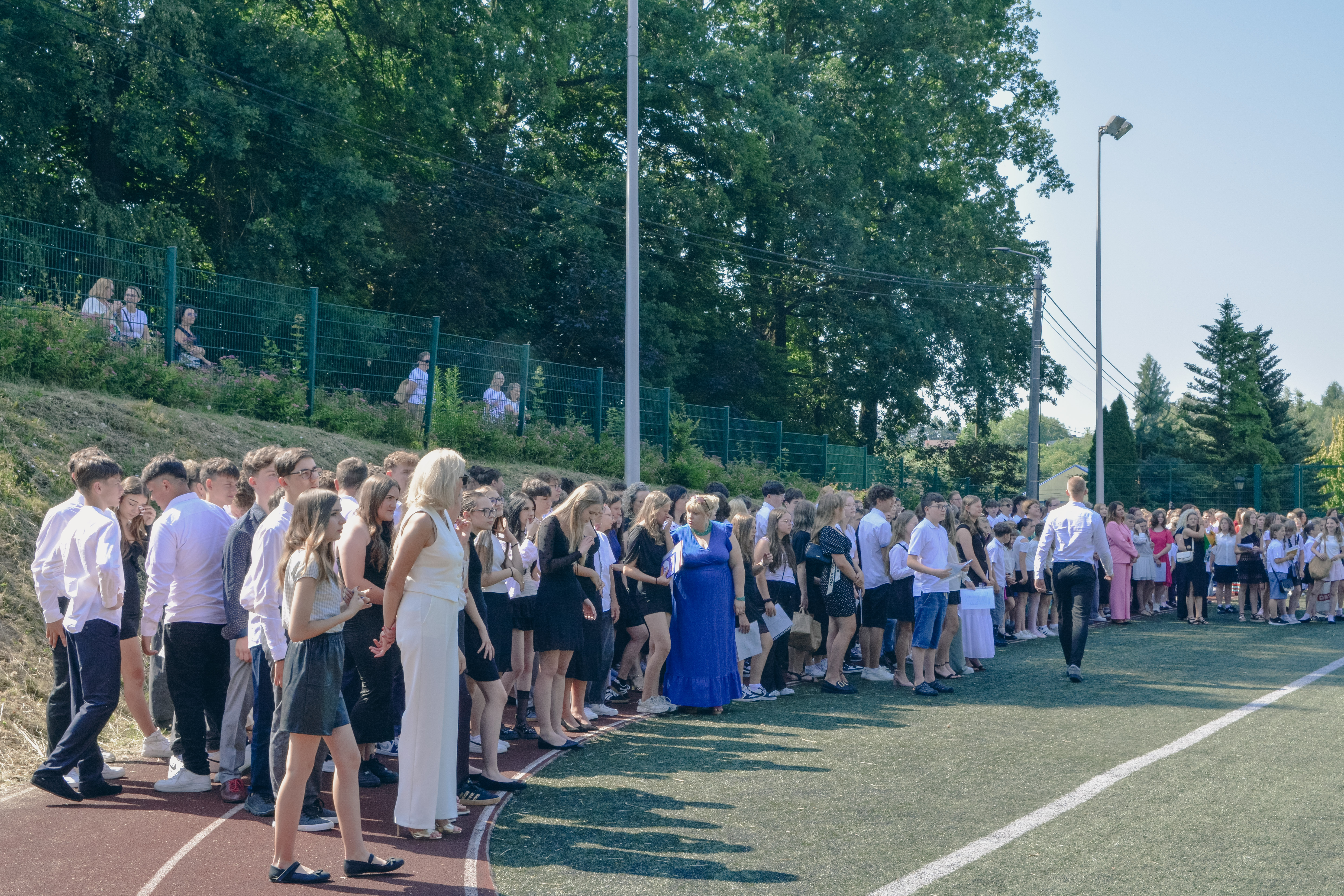 Duża grupa uczni&oacute;w zebranych na&nbsp;boisku szkolnym