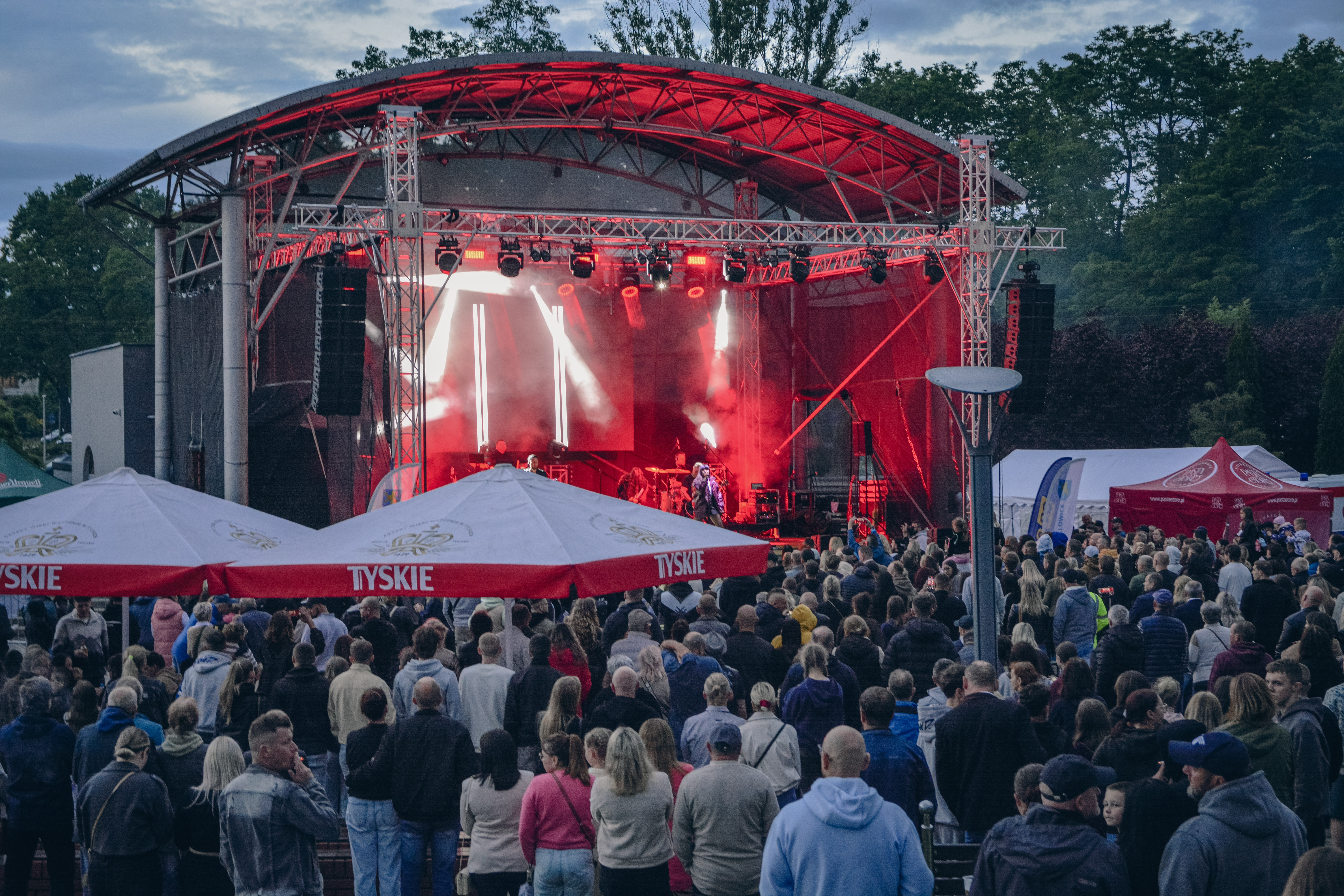 Widoczna scena z&nbsp;czerwonymi światłami, na&nbsp;scenie stoi postać z&nbsp;rękoma uniesionymi w&nbsp;g&oacute;rze, przed sceną tłum fan&oacute;w