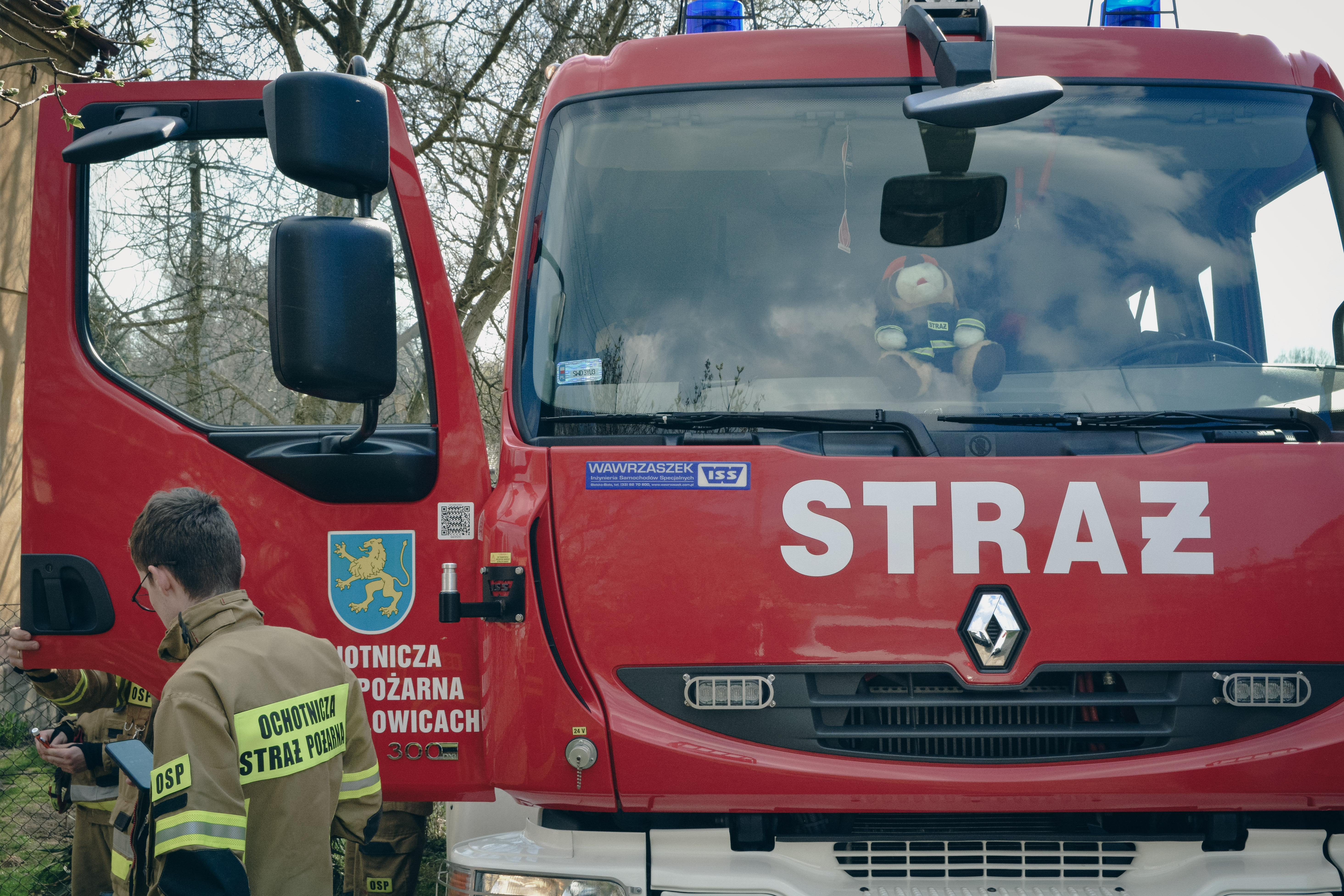 W&oacute;z bojowy straży bożarnej OSP Marklowice z&nbsp;przodu, na&nbsp;otwartych drzwiach samochodu herb Gminy Marklowice, strażak OSP przechodzi obok samochodu