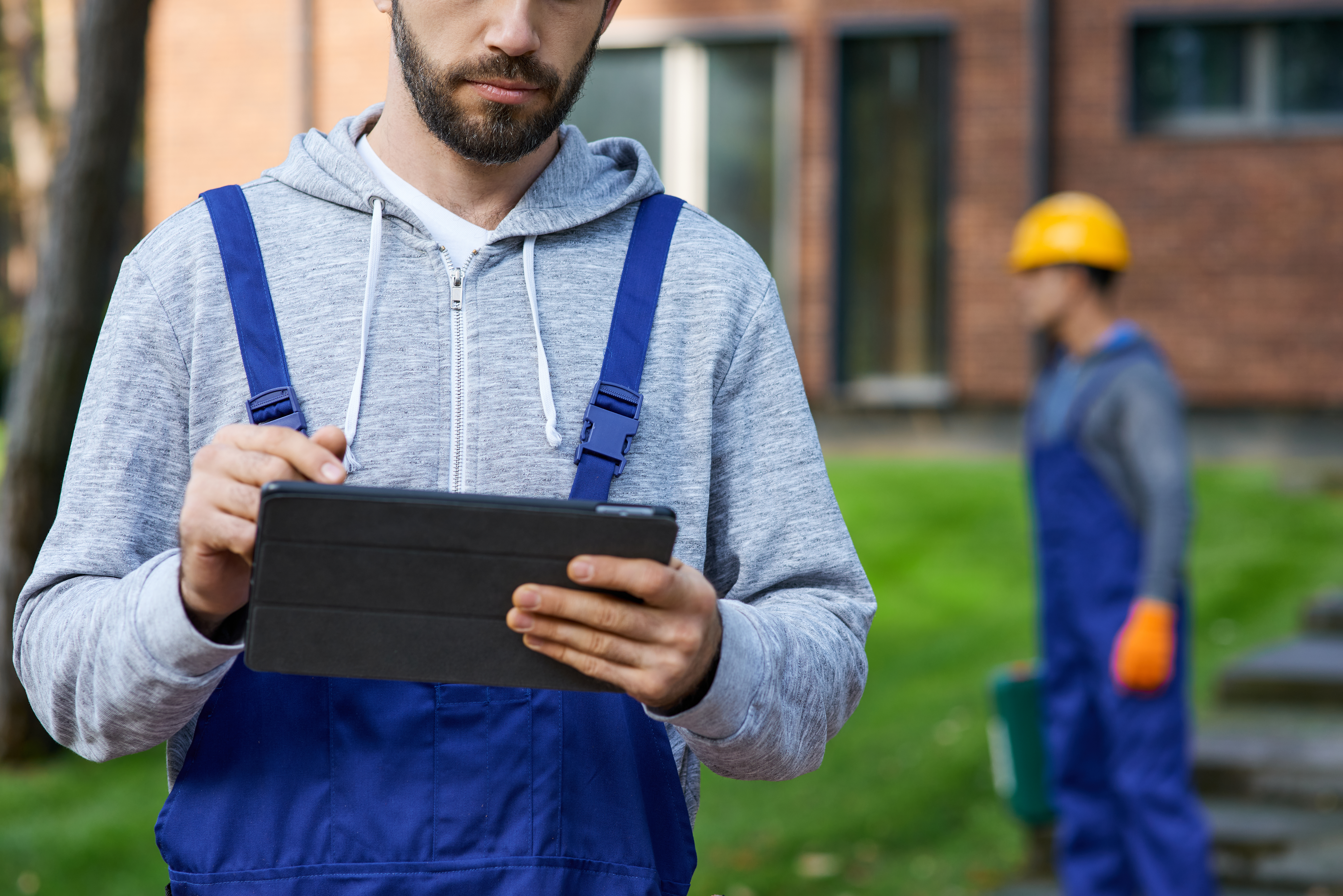 Pracownicy w&nbsp;ubraniach roboczych stoją przed domem, jeden z&nbsp;nich trzyma w&nbsp;rękach tablet