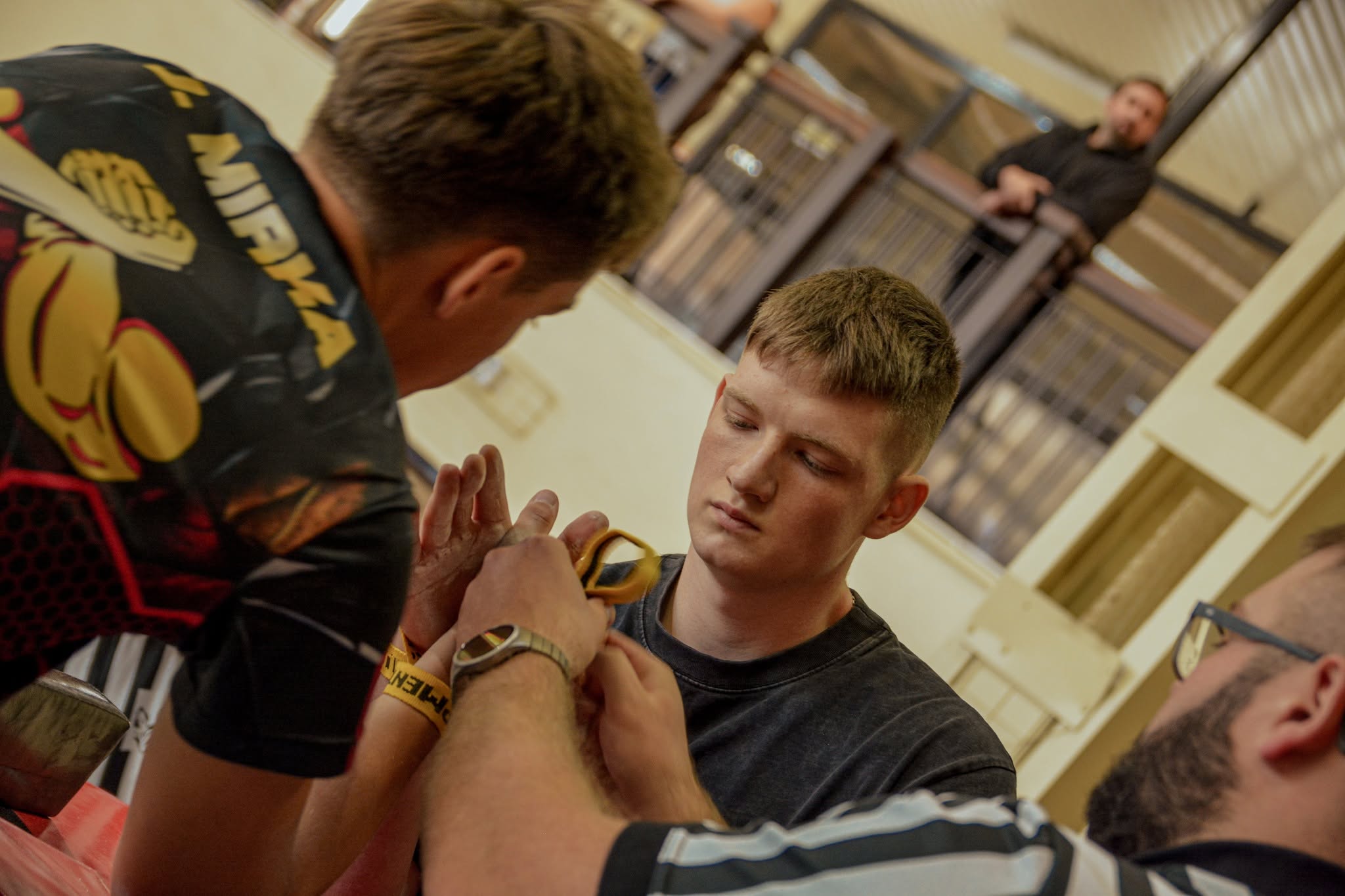 Dw&oacute;ch zawodnik&oacute;w armwrestlingu przygotowuje się do pojedynku chwytając się za dłonie, obok stoi sędzia
