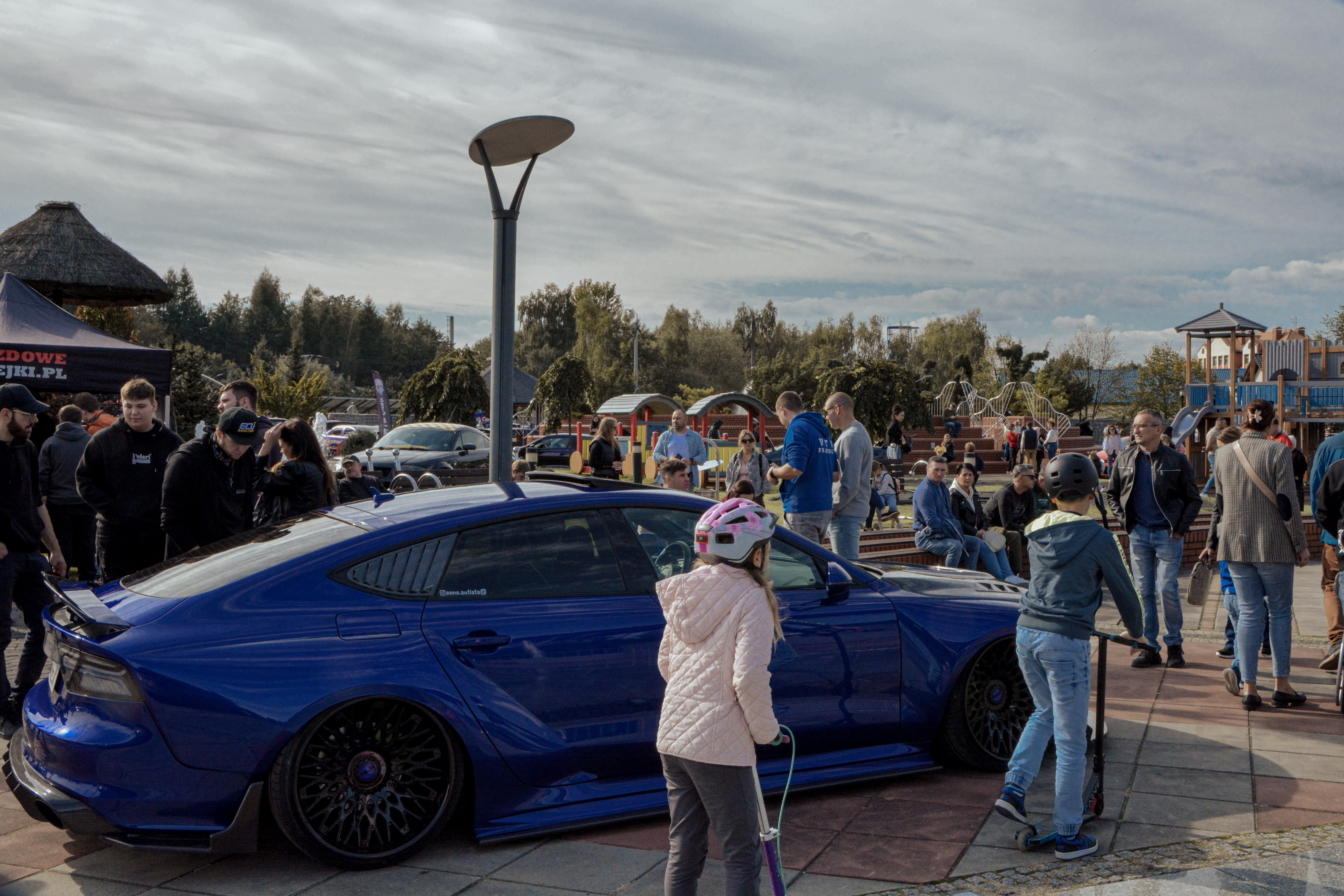Sportowe samochody stoją na&nbsp;parkingu zaparkowane podczas zlotu, tłum ludzi spaceruje podziwiając auta