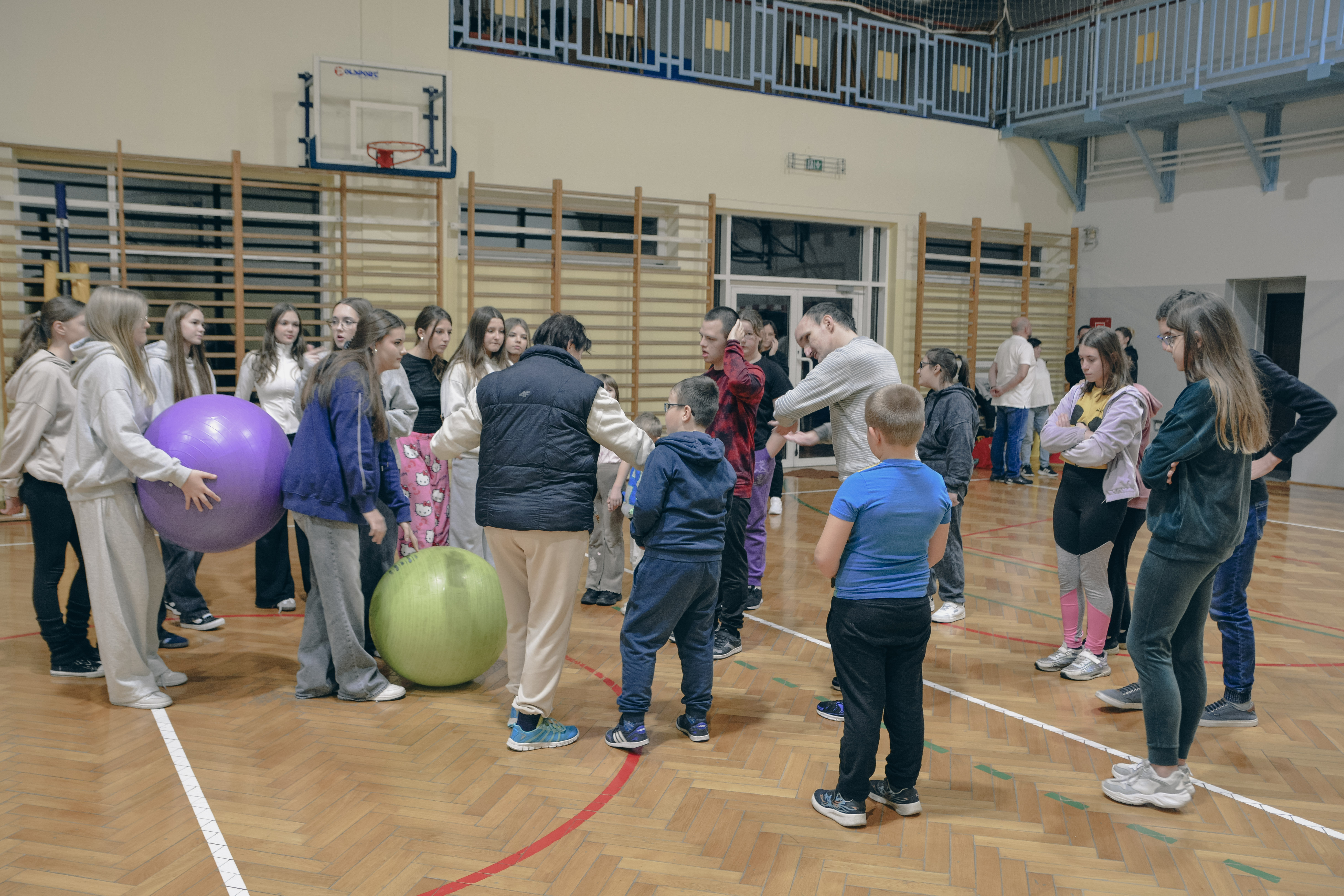 Grupa os&oacute;b na&nbsp;sali gimnastycznej przygotowuje się do zabaw sportowych