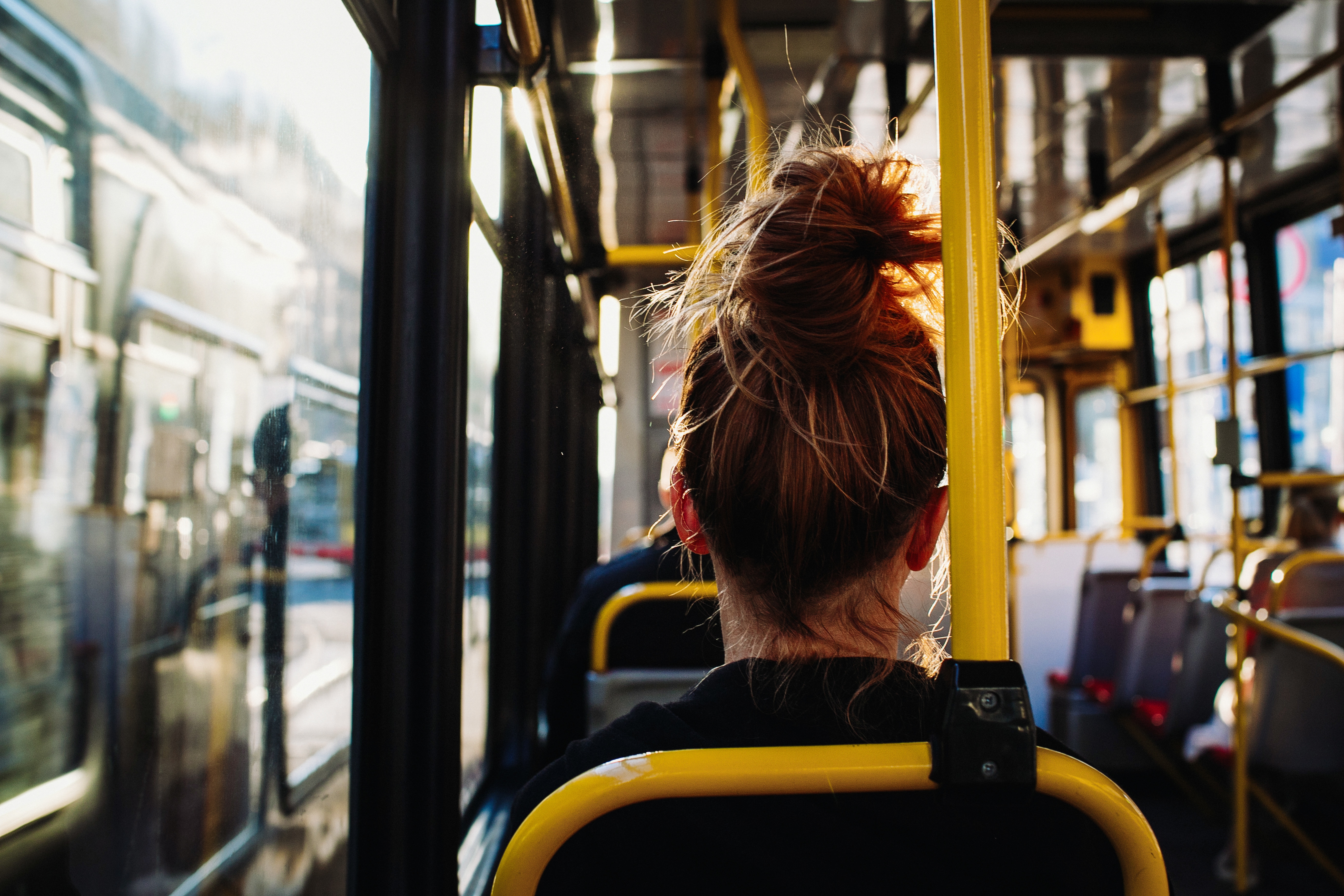 Wnętrze autobusu miejskiego, kobieta siedzi na&nbsp;fotelu tyłem do obiektywu