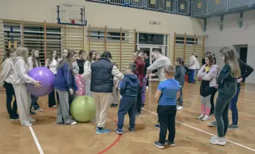 Grupa osób na sali gimnastycznej przygotowuje się do zabaw sportowych