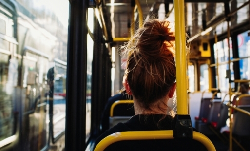 Wnętrze autobusu miejskiego, kobieta siedzi na fotelu tyłem do obiektywu