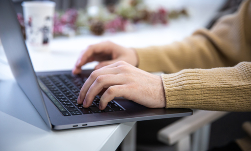 Zbliżenie na parę ludzkich rąk, które dotykają klawiatury laptopa, stojącego na brzegu stolika