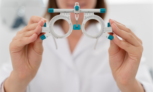 Osoba w białym kitlu trzyma przed sobą w dłoniach przyrząd optometryczny