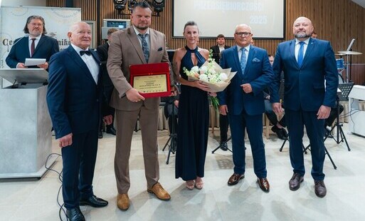 W pomieszczeniu do zdjecia pozuje kilka osób, jeden mężczyzna trzyma pamiątkową tabliczkę w wyróżnieniem dla firmy GRABARA DEVELOPMENT, kobieta trzyma bukiet kwiatów, obok władze powiatu i Gminy oraz prezes Cechu Rzemieślników