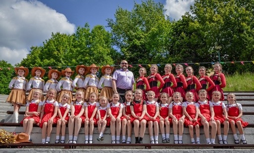 Duża grupa dziewcząt w różnym wieku i strojach z zespołu APLAUZ z Marklowic pozuje do zdjecia razem z Wójtem Gminy