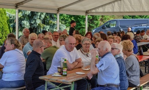 Uczestnicy wydarzenia Dzień Sąsiada w Marklowicach siedzą na ławkach pod dużym namiotem