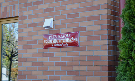 Fasada budynku z cegły z tabliczką z napisem "Przedszkole Akademia Wyobraźni w Marklowicach"