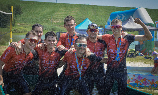 7 mężczyzn w czerwono-czarnych strojach sportowych pozuje do zdjecia w basenie z wodą podczas wydarzenia Bike Race & Szanty