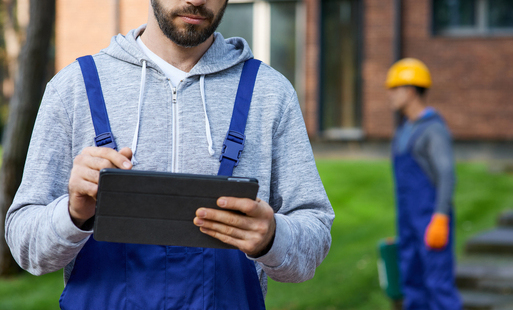 Pracownicy w ubraniach roboczych stoją przed domem, jeden z nich trzyma w rękach tablet