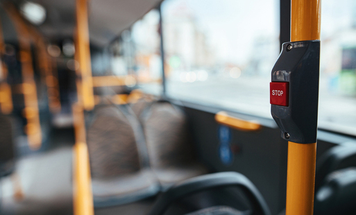 Puste wnętrze autobusu z widocznymi siedziskami oraz przyciskiem STOP na żółtym słupku