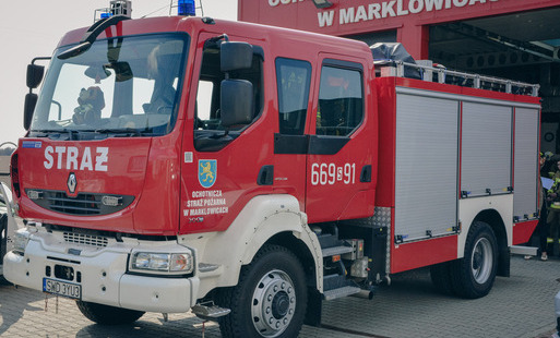 Czerwony wóz strażacki stoi przed remizą z napisem Ochotnicza Straż Pożarna w Marklowicach