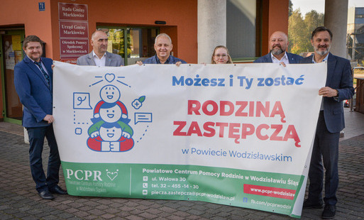 Kilka osób stoi przed budynkiem Urzędu Gminy w Marklowicach, trzymając rozwinięty duży baner promocyjny o rodzinach zastępczych